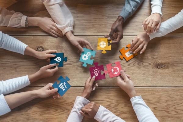 A circle of hands holding puzzle pieces with symbols on them
