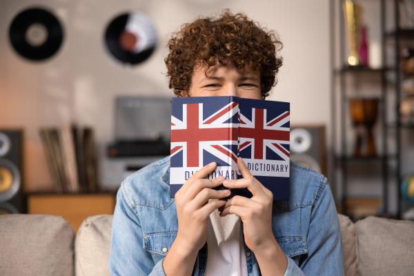 Young person holding an English language dictionary in front of his face