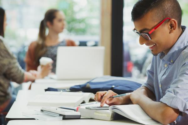 Young person smiling whilst using a calculator at a desk