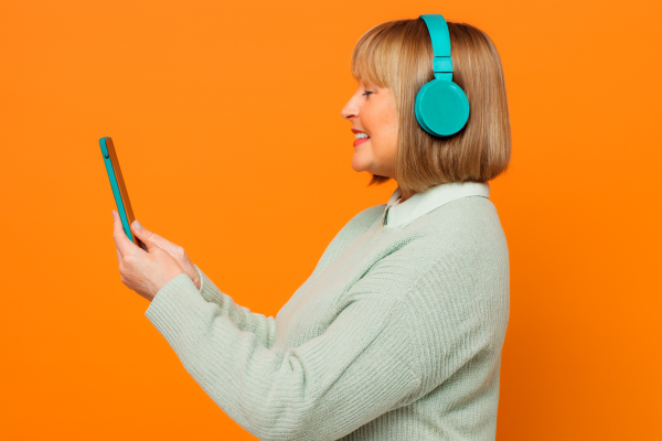 smiling woman wearing headphones and looking at a phone