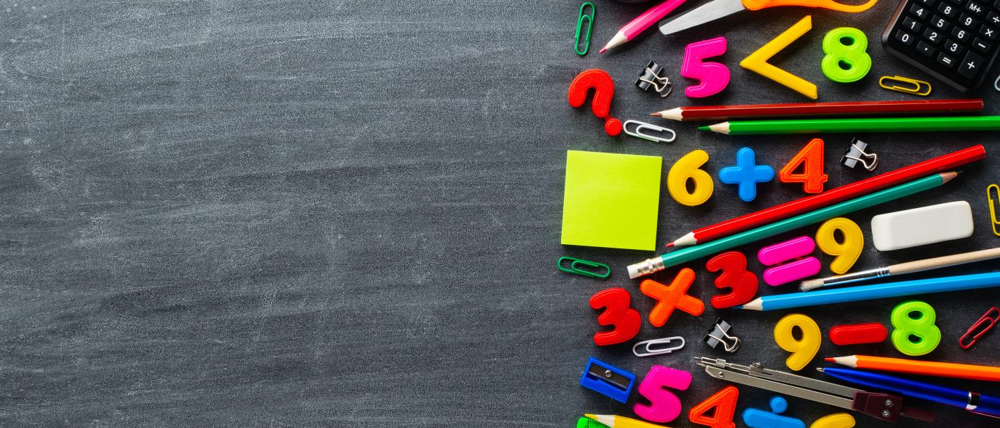 Brightly coloured numbers, calculator and stationery items on a blackboard