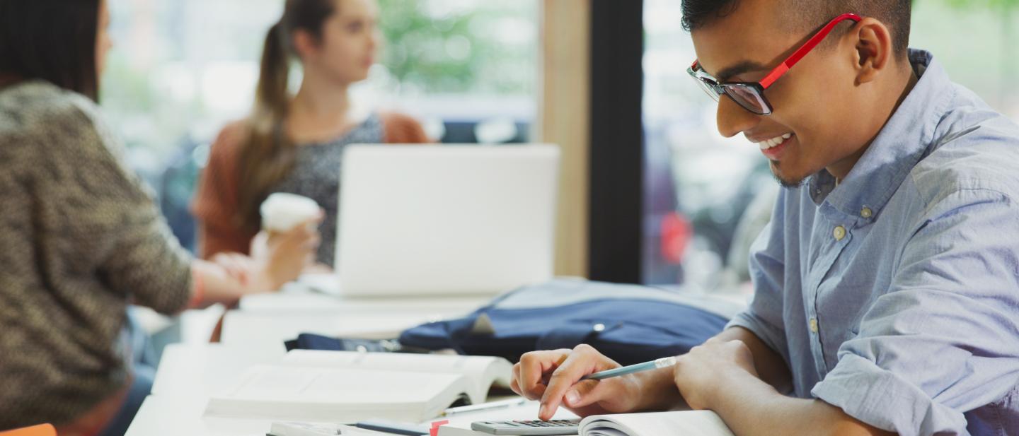Young person smiling whilst using a calculator at a desk