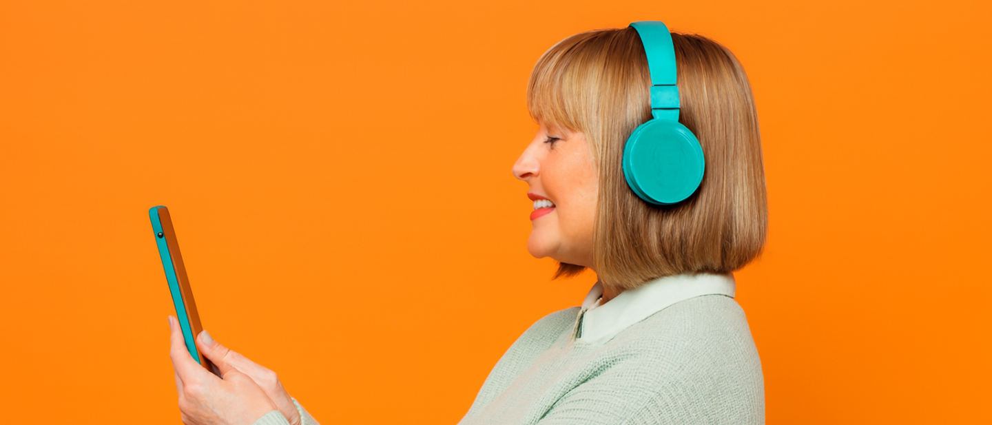 smiling woman wearing headphones and looking at a phone